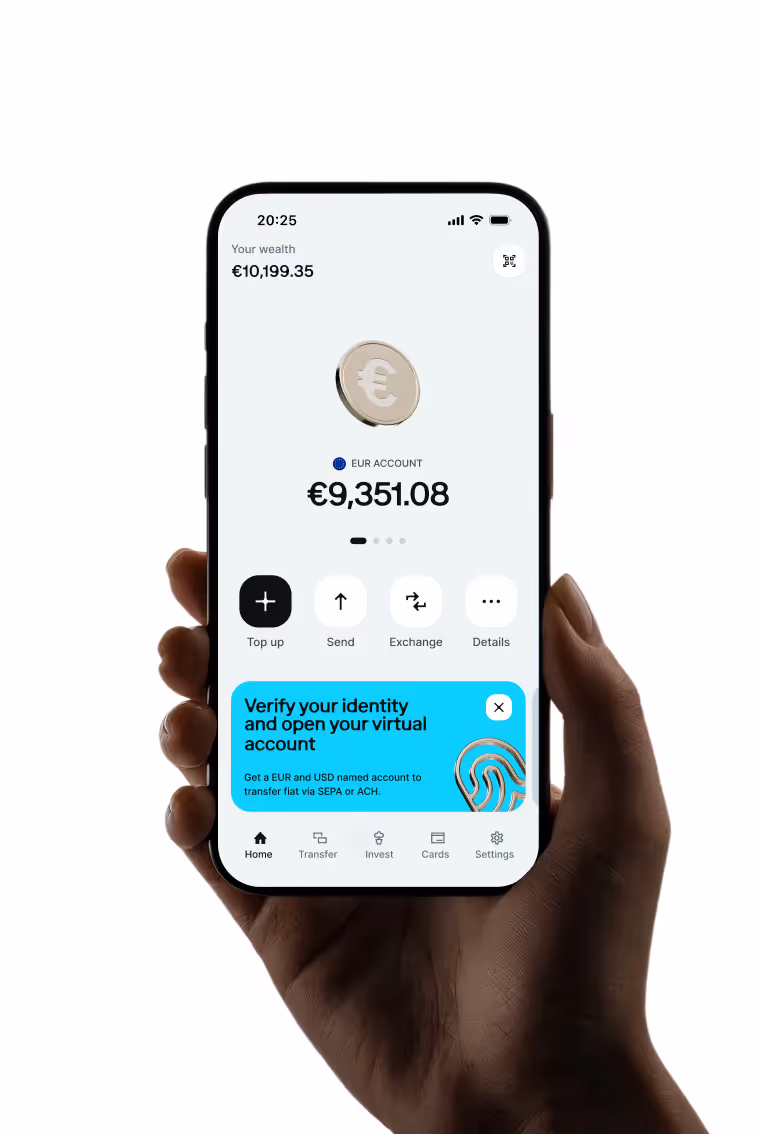 Mano che tiene uno smartphone con un'app bancaria che mostra un saldo del conto in EUR di 9.351,08 € e un patrimonio totale di 10.199,35 €, con le opzioni per ricaricare, inviare, cambiare e vedere i dettagli, oltre a una notifica blu che invita a verificare l'identità e ad aprire un conto virtuale.