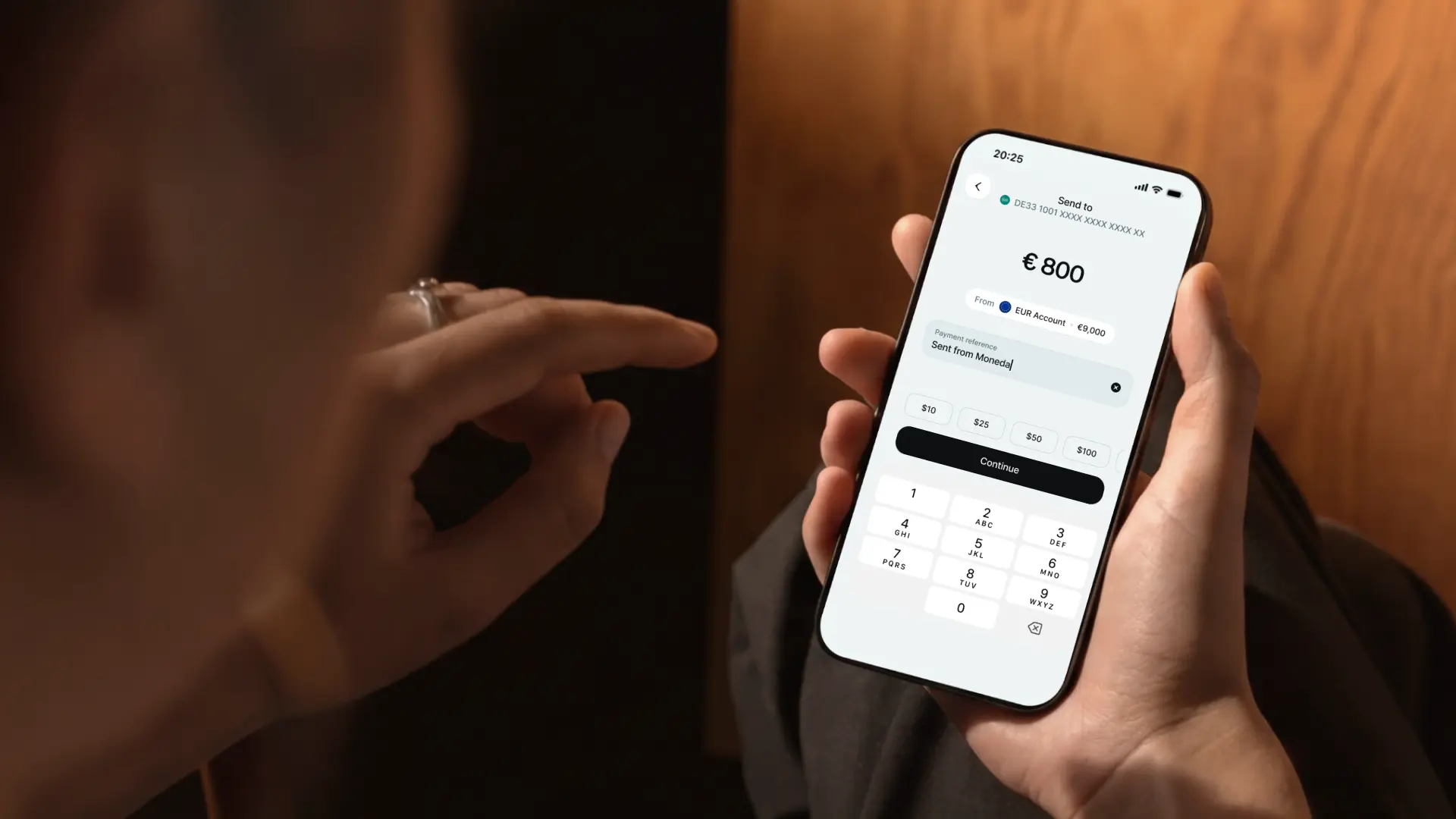 A hand holding a phone with the Moneda send screen, a payment of €800 with a payment reference entered